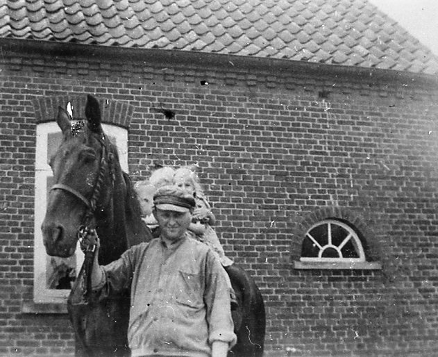 Müller Hinrichs hält dunkles Pferd am Zaumzeug, 3 Kleinkinder auf dem Pferderücken vor dem Müllerhaus / 1948