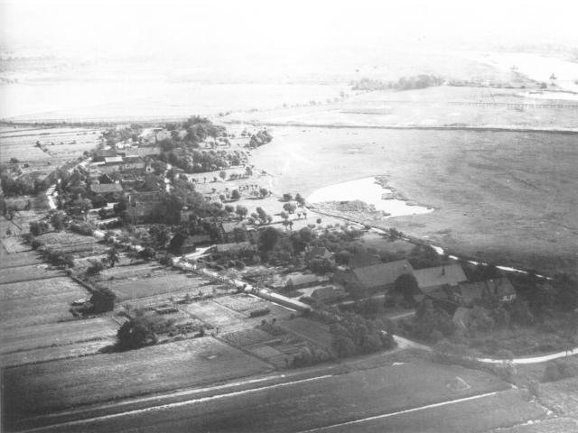 Ansicht vom ehemaligen Mittelsbüren von der Landseite. Die Höfe lagen dicht aneinander hinter dem Deich. Am Groden entlang fließt die Lake, die im letzten Jahrhundert auch als Trinkwasservorrat diente. Die Lake war ein Graben, der sich am Dorfe hinzog und der sich bei Flut mit Weserwasser füllte. Durch ein Siel mit einer Stauvorrichtung wurde das Wasser bei Ebbe zurückgehalten, so daß jederzeit Weserwasser daraus zu holen war. Aus der "Pottkuhle" wurde in früheren Zeiten Lehm für die Deiche entnommen. Im Winter konnten die Kinder dort Schlittschuhlaufen. Im Hintergrund sieht man in der Baumgruppe die Ortschaft Osterort. / Foto: Westd. Luftfoto Bremen