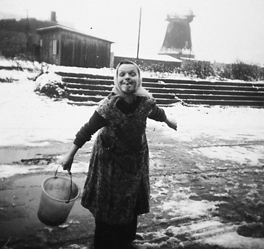 Mühle im Hintergrund, Frau mit Eimer steckt Zunge raus ca. 1953