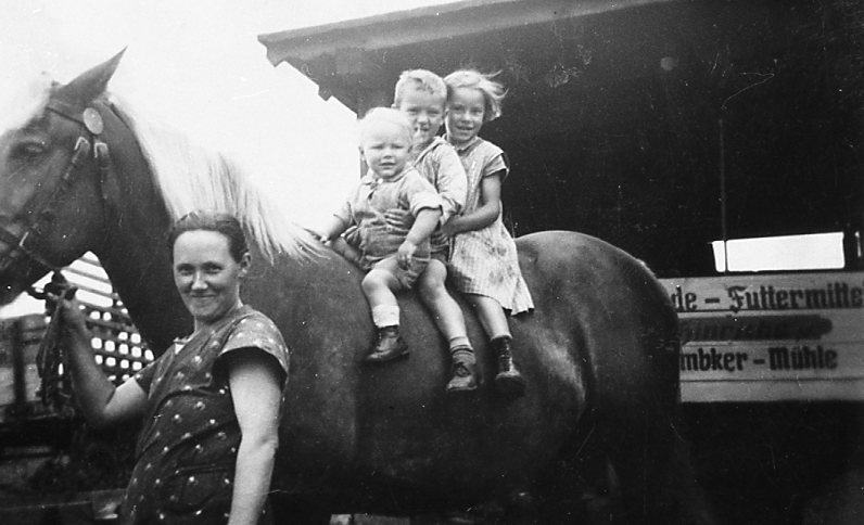 Frau hat Pferd am Zaum, 3 Kinder auf dem Pferderücken